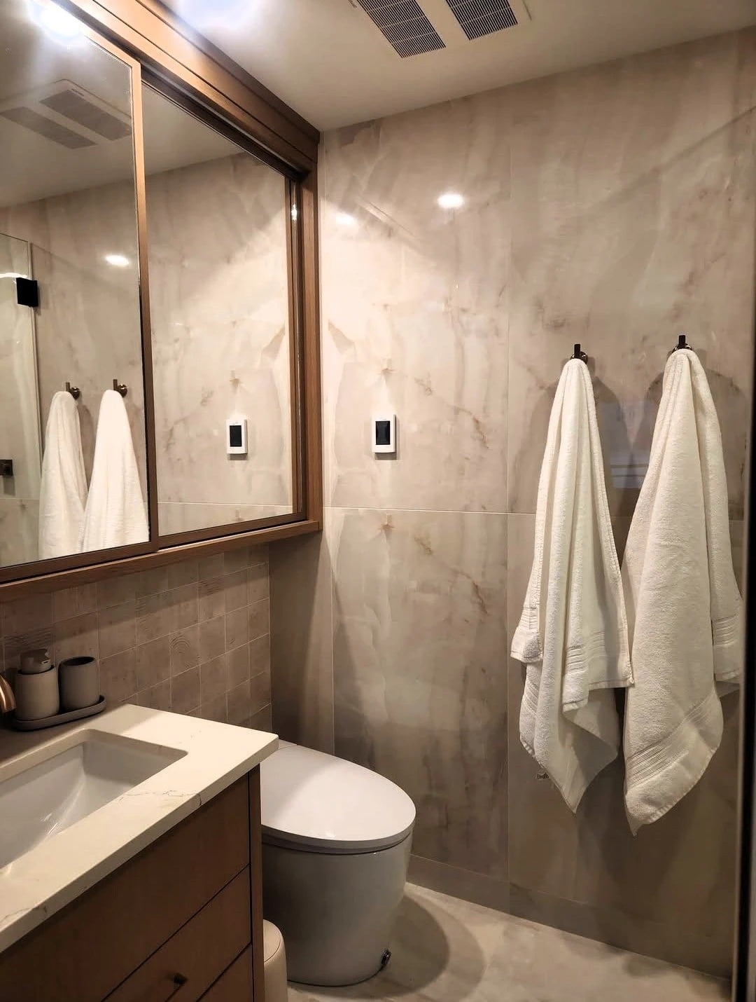 Modern bathroom with marble tile walls, vanity and mirror, and white towels