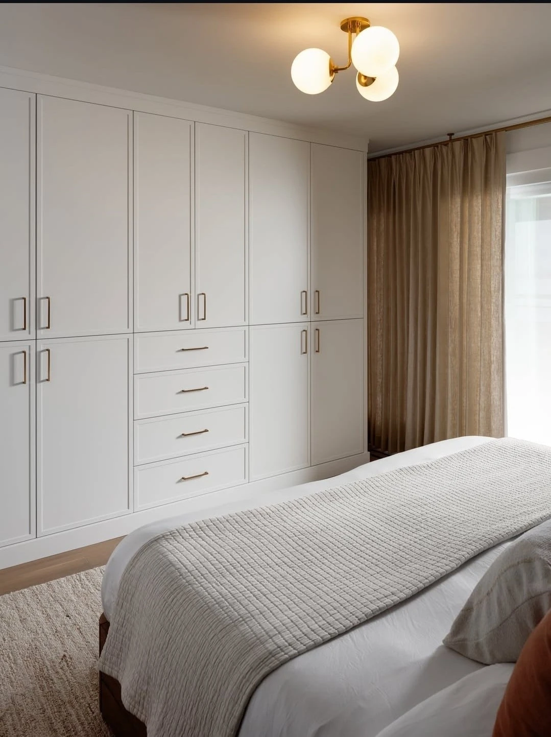Stellar Craft Cabinetry Inc. built-in white and gray cabinet wall in a modern bedroom with dresser-style drawers and brass lighting